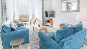 Ein geräumiges Wohnzimmer mit großem Fenster, Fernseher und blau gepolsterten Möbeln.
