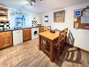 A compact kitchen with wooden cabinets, a dishwasher, a washing machine, and a dining table with chairs. - Cosy and relaxing holiday house. (Ansturther)