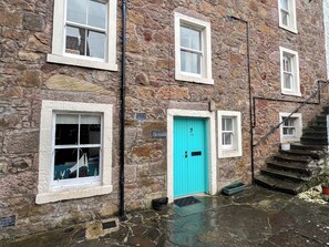 Un bâtiment en pierre doté de nombreuses fenêtres, d’une porte turquoise et d’un escalier menant à un étage supérieur.