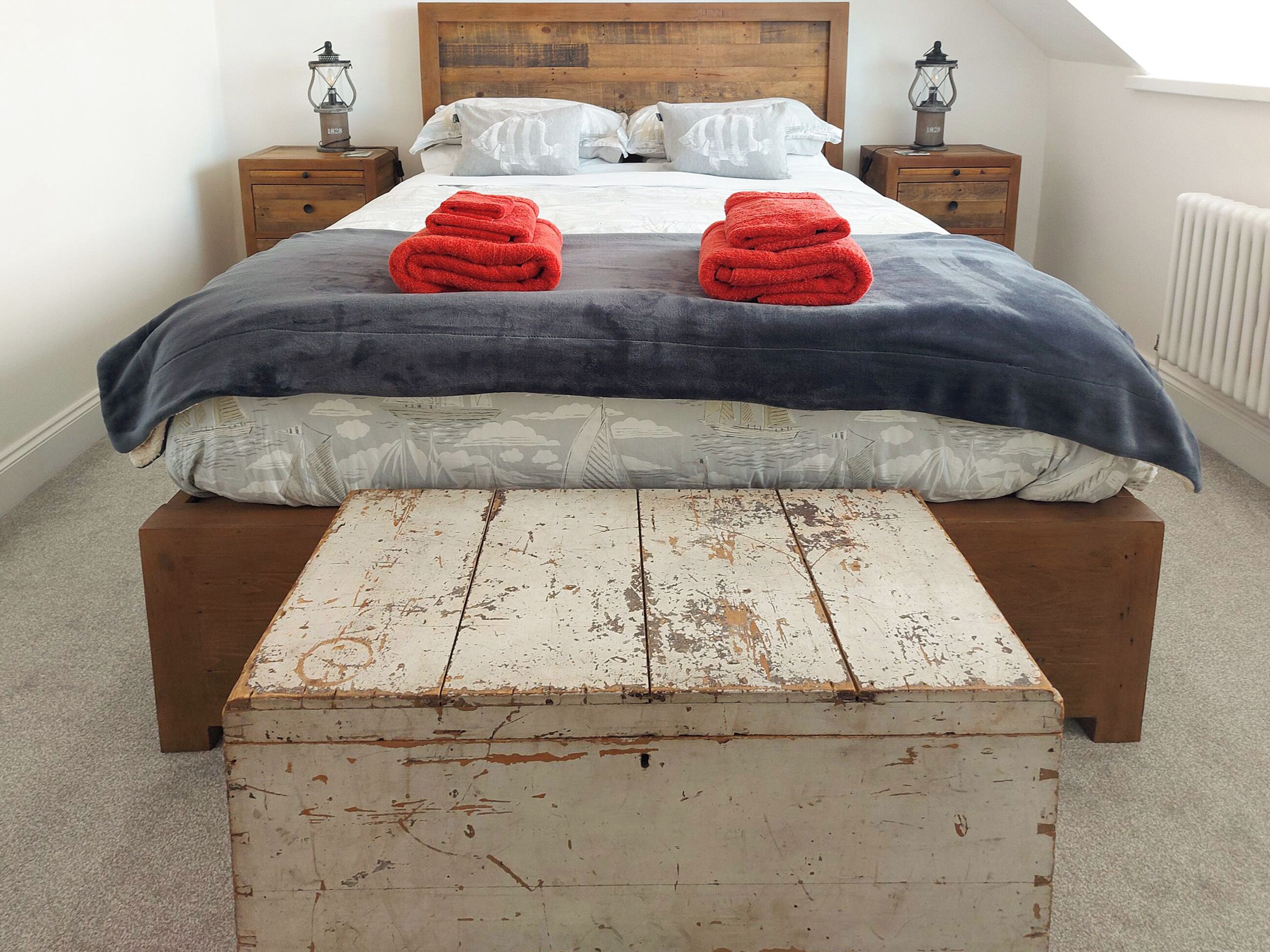 A neatly made bed with two red towels, a wooden headboard, and a rustic chest of drawers.