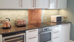Une cuisine avec des meubles blancs, un four en acier inoxydable, un four à micro-ondes, un grille-pain et une bouilloire.