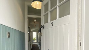 Un couloir avec une porte blanche portant le numéro 2, une sonnette bleue et un luminaire au-dessus de la porte.