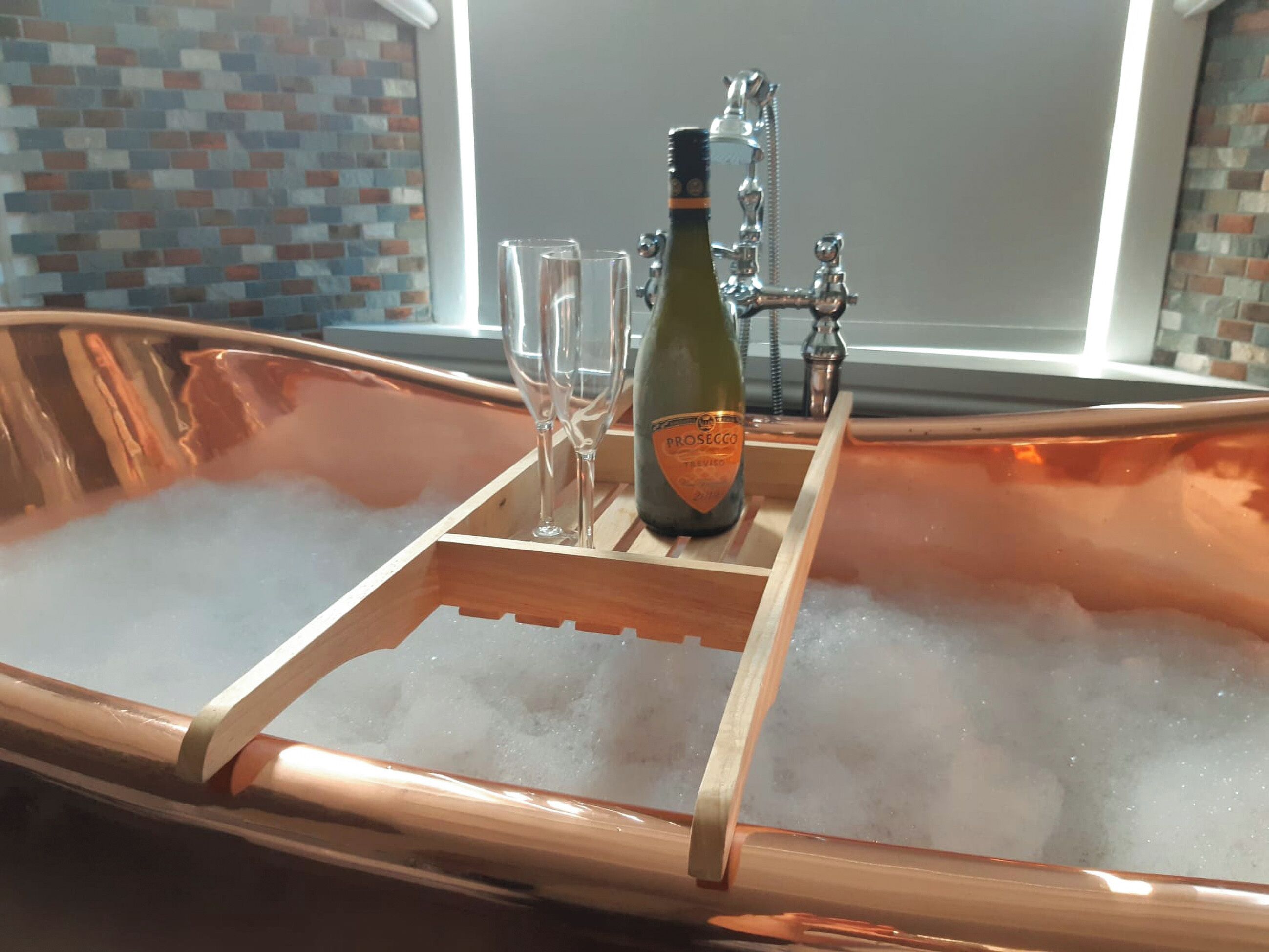 A copper bathtub filled with ice, a bottle of Prosecco, and two glasses.