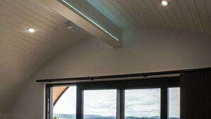 Une pièce dotée d’un plafond en pente, d’un éclairage encastré et de grandes fenêtres offrant une vue sur le paysage.