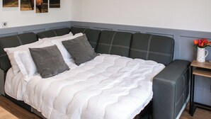 Une chambre à coucher avec un lit, des oreillers, une table de chevet, un vase avec des fleurs et trois tableaux accrochés au mur.
