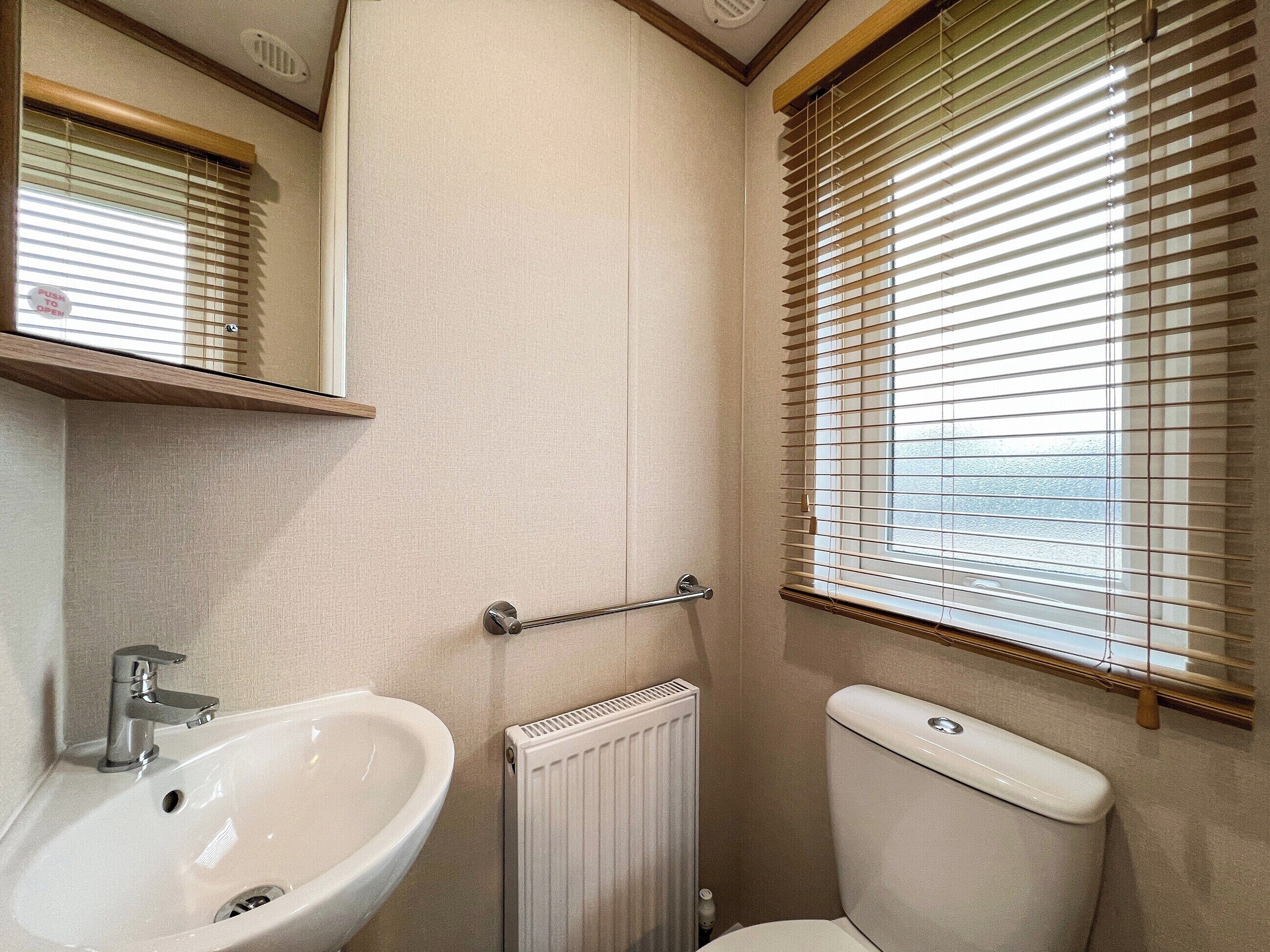 Ein Badezimmer mit Waschbecken, Toilette und Fenster mit Jalousien.
