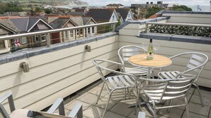 Terraza en la azotea con una mesa redonda y cuatro sillas, con vistas a un pueblo costero.