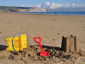 Ein Sandstrand mit einem gelben Sandkasten-Eimer, einer roten Schaufel und einer Sandburg-Konstruktion.