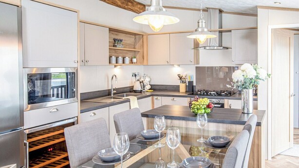 Una cocina moderna con una isla central, electrodomésticos integrados y un comedor con mesa de vidrio y sillas tapizadas en gris.