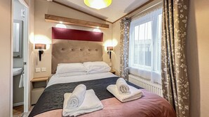 A hotel room with a bed, two bedside lamps, a window with curtains, and a headboard. - Cute, cosy and warm. (St Andrews)