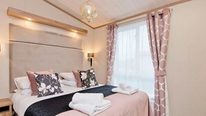 Une chambre à coucher avec un lit, des tables de chevet, une lampe fixée au mur et une fenêtre avec des rideaux.