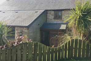 A stone house with a sloped roof and a wooden fence in the foreground. - Fistral Cottage - CWC46839 (Perranporth)