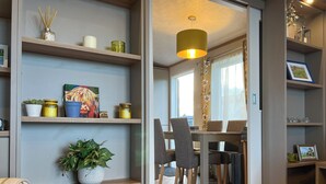 A modern living room with wooden shelves, a dining area with a table and chairs, and a large window with curtains. - 2 bedroom accommodation in St Andrews (St Andrews)
