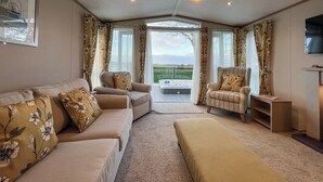 A cozy living room with a sofa, armchairs, and a large window offering a view of the outdoors. - 2 bedroom accommodation in St Andrews (St Andrews)