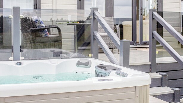 Ein Whirlpool mit Glasverkleidung, eine Sitzgelegenheit im Freien mit Korbmöbeln und ein Gebäude mit einer Schiebetür.