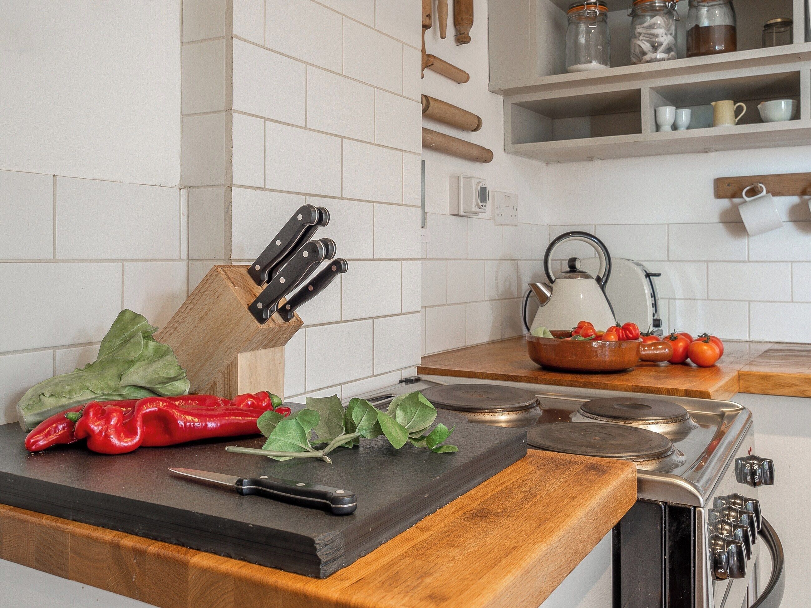 A kitchen counter with a cutting board, a knife, and a knife block. There are tomatoes and lettuce on the counter.