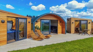 Eine moderne Holz-Blockhütte mit gewölbtem Dach, großen Glasüren und einer Terrasse mit Sitzgelegenheit.