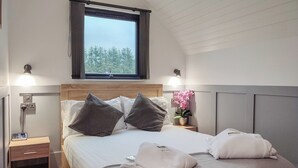 Ein ordentlich eingerichtetes Schlafzimmer mit einem Holzkopfende, einem Nachttisch mit Lampe und einem Fenster mit Blick auf Bäume.