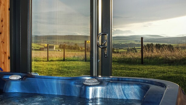 Ein Whirlpool mit Blick auf eine ländliche Landschaft durch große Fenster.