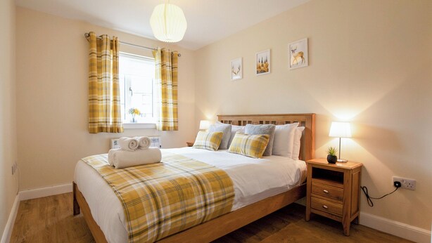 Een slaapkamer met een houten bed, een nachtkastje met een lamp en een raam met gordijnen.