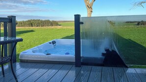 Ein Whirlpool auf einer Holzdiele mit Glastür, umgeben von einer grünen Wiese und einem Baum.