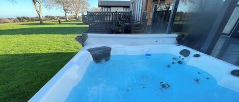 Un jacuzzi con superficie de agua azul cristalina, rodeado por una terraza de madera y un césped.