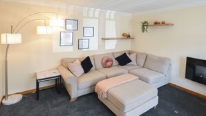 A modern living room with a sectional sofa, a floor lamp, framed artwork, and a TV on the wall. - 3 bedroom accommodation in Fort William (Fort William)