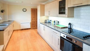 A kitchen with wooden cabinets, a black countertop, and a tiled backsplash. - 3 bedroom accommodation in Fort William (Fort William)