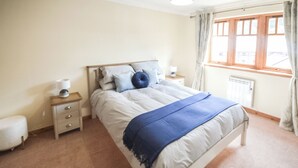 A bedroom with a bed, bedside tables, a lamp, a radiator, and a window with curtains. - 3 bedroom accommodation in Fort William (Fort William)