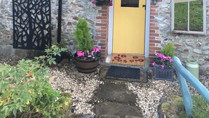A stone building with a yellow door, a black decorative panel, and potted plants. - 1 bedroom accommodation in Wooton Fitzpaine, near Charmouth (Wooton Fitzpaine, near Charmouth)