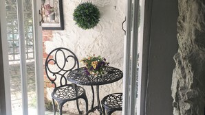 A small outdoor seating area with a round table and two chairs, a hanging plant, and a wall-mounted mirror. - 1 bedroom accommodation in Wooton Fitzpaine, near Charmouth (Wooton Fitzpaine, near Charmouth)