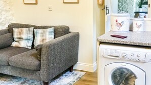 A living room with a gray sofa and a washing machine in the background. - 1 bedroom accommodation in Wooton Fitzpaine, near Charmouth (Wooton Fitzpaine, near Charmouth)