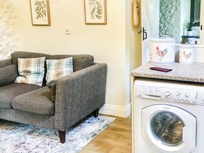 Ein Wohnzimmer mit grauem Sofa und einer Waschmaschine im Hintergrund.