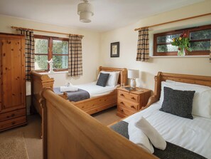 A bedroom with two single beds, a wooden wardrobe, a bedside table with a lamp, and a window with curtains. - A wonderful retreat for two couples or a family to enjoy. (Wooton Fitzpaine, near Charmouth)