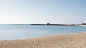 A pebbled beach with a calm sea, a pier extending into the water, and a few buildings in the distance. - 3 bedroom accommodation in Wooton Fitzpaine, near Charmouth (Wooton Fitzpaine, near Charmouth)