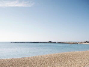 A pebbled beach with a calm sea, a pier extending into the water, and a few buildings in the distance. - 3 bedroom accommodation in Wooton Fitzpaine, near Charmouth (Wooton Fitzpaine, near Charmouth)