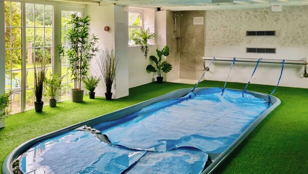 An indoor swimming pool with a blue pool cover, surrounded by potted plants and a green artificial turf area. - 3 bedroom accommodation in Wooton Fitzpaine, near Charmouth (Wooton Fitzpaine, near Charmouth)