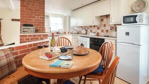 A cozy kitchen with a brick wall, wooden table, and chairs. There is a microwave, oven, and a clock on the wall. - 3 bedroom accommodation in Wooton Fitzpaine, near Charmouth (Wooton Fitzpaine, near Charmouth)