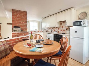 A cozy kitchen with a brick wall, wooden table, and chairs. There is a microwave, oven, and a clock on the wall. - 3 bedroom accommodation in Wooton Fitzpaine, near Charmouth (Wooton Fitzpaine, near Charmouth)