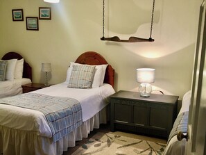Ein Hotelzimmer mit zwei Einzelbetten, einem Nachttisch mit Lampe, einem Hängekorbstuhl und drei gerahmten Bildern an der Wand.