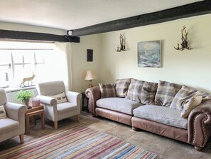 Ein Wohnzimmer mit einem beigefarbenen Sofa, einem weißen Sessel, einem kleinen Tisch mit einer Pflanze und einem Streifen Teppich.