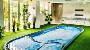 An indoor swimming pool with a green artificial turf surrounding it, potted plants, and a shower area. - 5 bedroom accommodation in Wooton Fitzpaine, near Charmouth (Wooton Fitzpaine, near Charmouth)