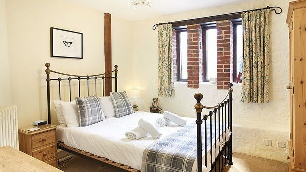 A bedroom with a four-poster bed, a bedside table, a nightstand, a wooden dresser, a window with curtains, and a framed picture on the wall. - 5 bedroom accommodation in Wooton Fitzpaine, near Charmouth (Wooton Fitzpaine, near Charmouth)