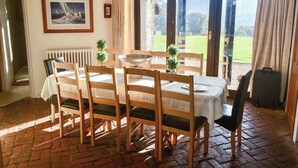 A dining area with a table set for six, wooden chairs, a white tablecloth, a framed picture on the wall, and a view of a green landscape through the glass door. - 5 bedroom accommodation in Wooton Fitzpaine, near Charmouth (Wooton Fitzpaine, near Charmouth)