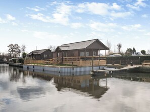A wooden building with a dock extending into calm water, surrounded by a fence and trees. - A water’s edge setting in the heart of the Norfolk Broads National Park. (Brundall)