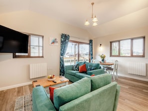 A modern living room with a sofa set, a coffee table, a TV, and a dining area with a table and chairs. - A water’s edge setting in the heart of the Norfolk Broads National Park. (Brundall)