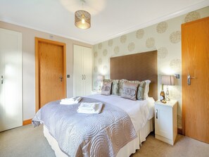 A neatly arranged bedroom with a large bed, a bedside table with a lamp, and a wardrobe. - 2 bedroom accommodation in Glanrafon Uchaf (Glanrafon Uchaf)