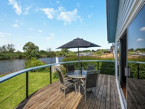 A wooden deck with a table and chairs, overlooking a river and greenery. - A perfect waterside setting. (Brundall)