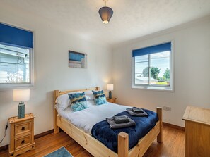 Ein Schlafzimmer mit einem hölzernen Bett, zwei Nachttischen, einer Wandlampe und zwei Fenstern mit blauen Jalousien.