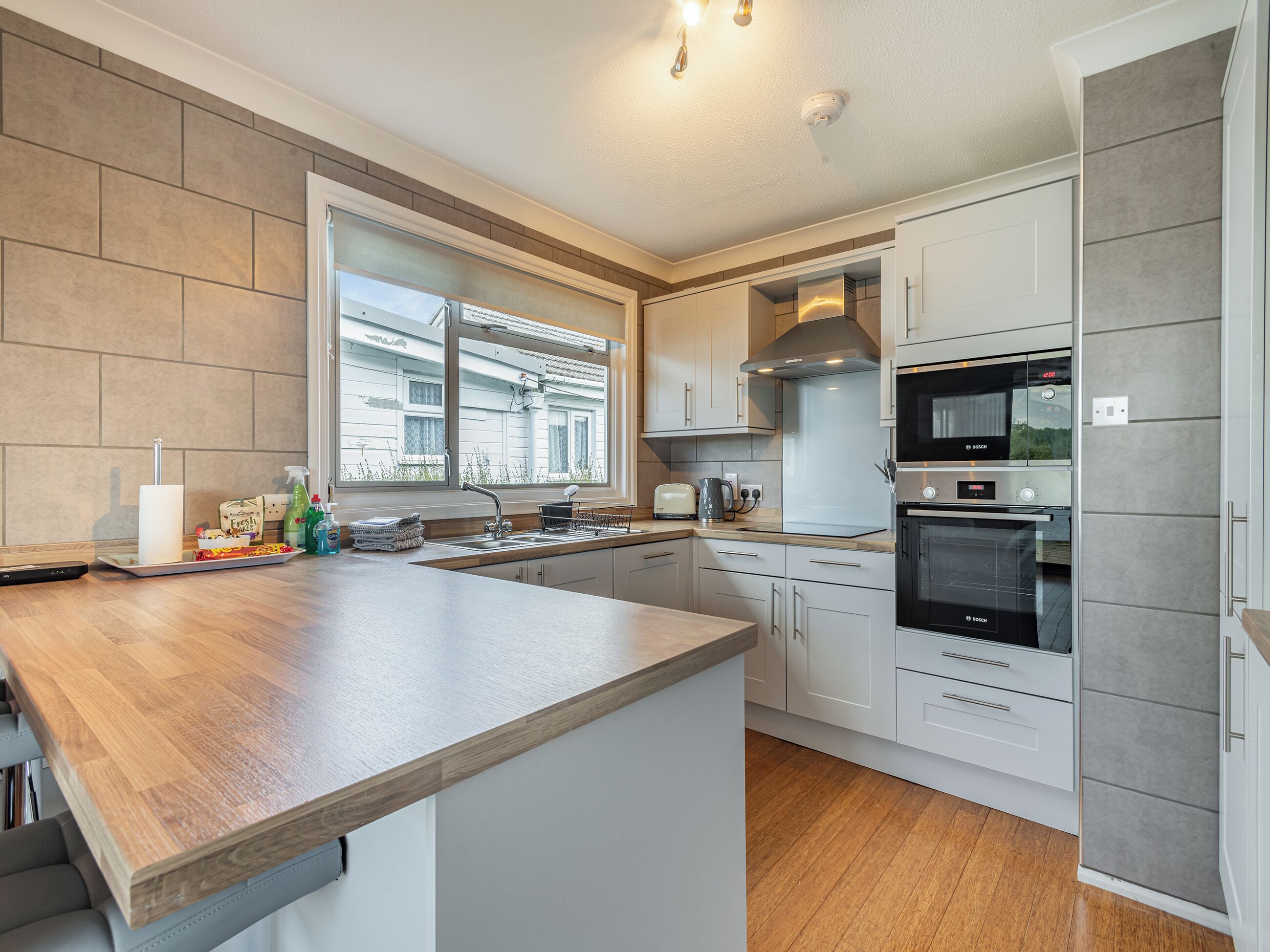 A modern kitchen with a wooden countertop, white cabinets, a Bosch oven, and a window providing natural light.